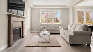 A living room with a fireplace, a sofa, a coffee table, and large windows. - A Beautiful Home in Airdrie (Airdrie)