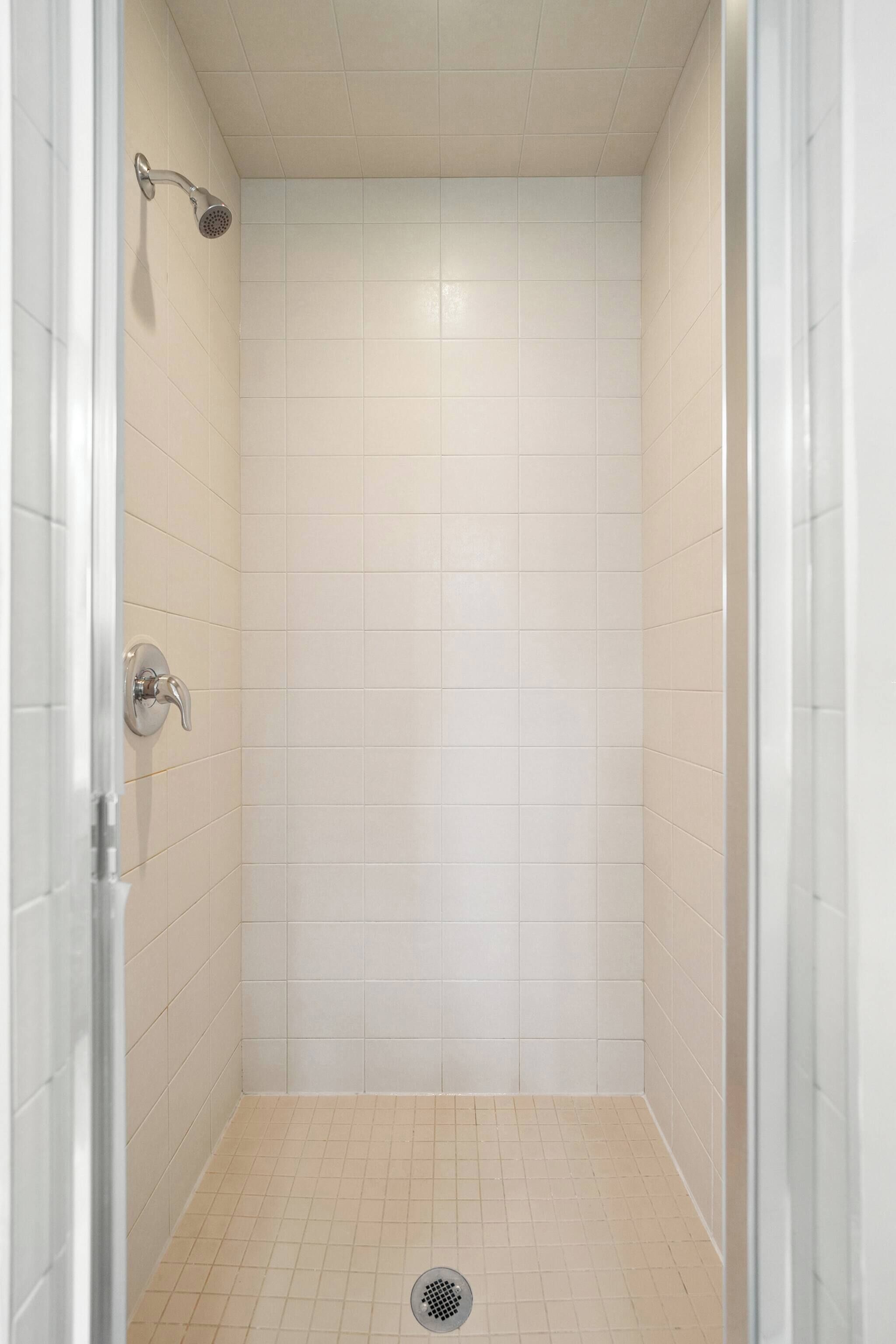 A small, enclosed shower area with white tiles and a showerhead.