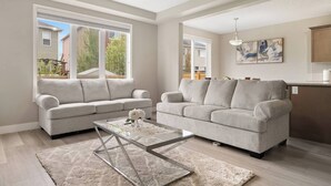 A spacious living room with two grey sofas, a glass coffee table, and a large window providing a view of the outside. - A Beautiful Home in Airdrie (Airdrie)