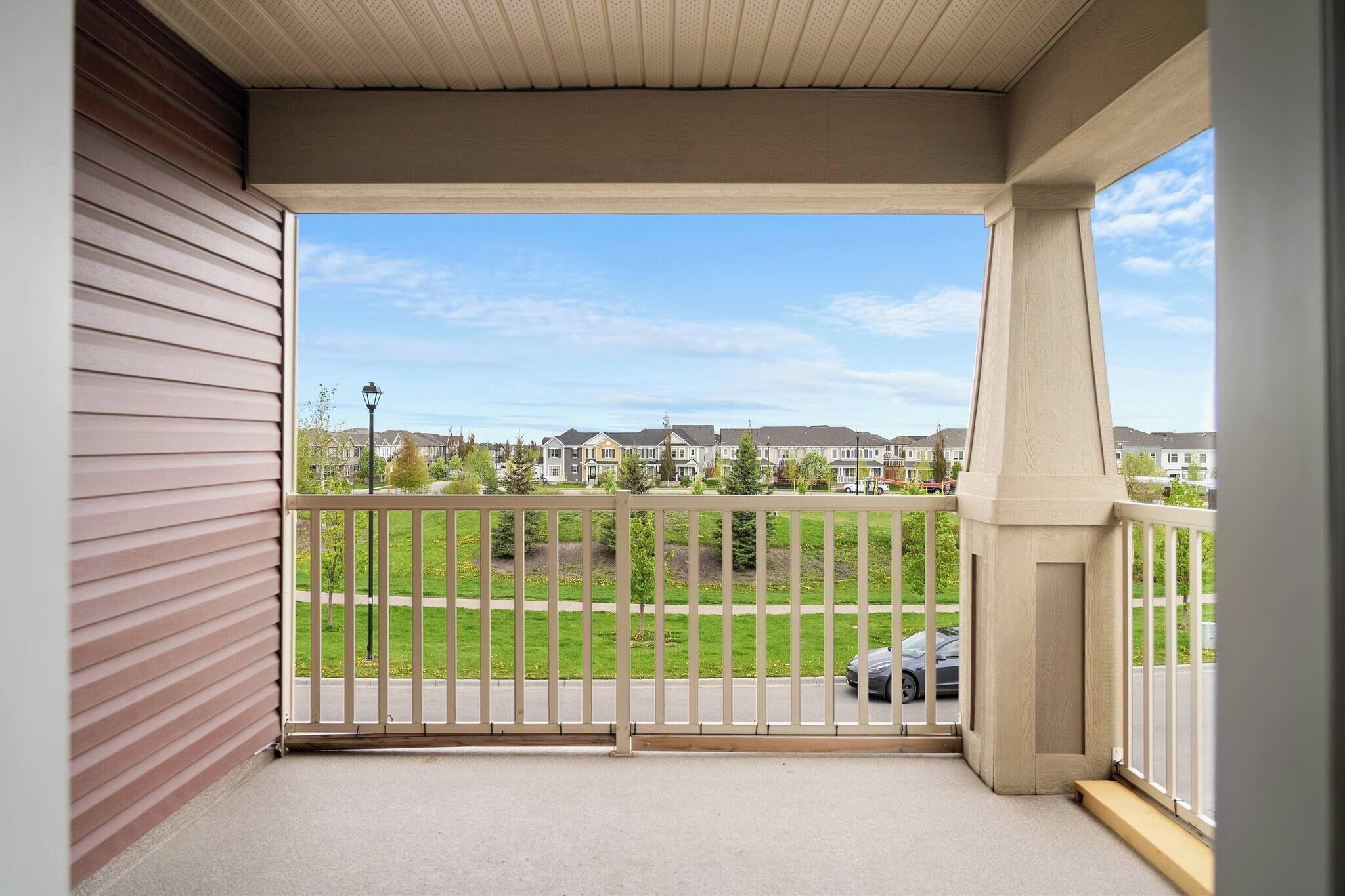 Ein Balkon mit Blick auf ein Wohngebiet, einen Zaun und ein parkendes Auto.