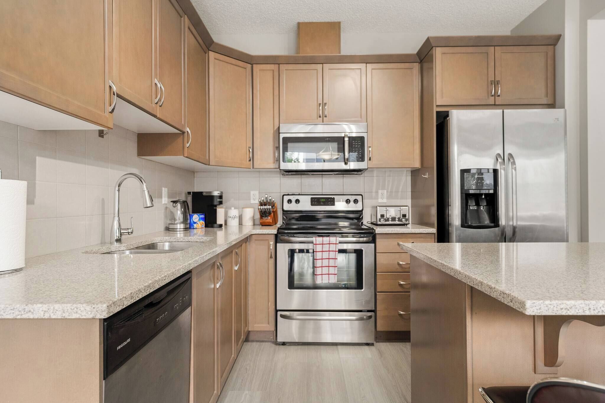 A modern kitchen with wooden cabinets, stainless steel appliances, a dishwasher, and a granite countertop.