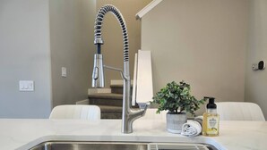 A modern kitchen with a stainless steel sink, a high-arc faucet, a potted plant, and a bottle of hand soap. - Harmony Haven in Drumheller (Drumheller)