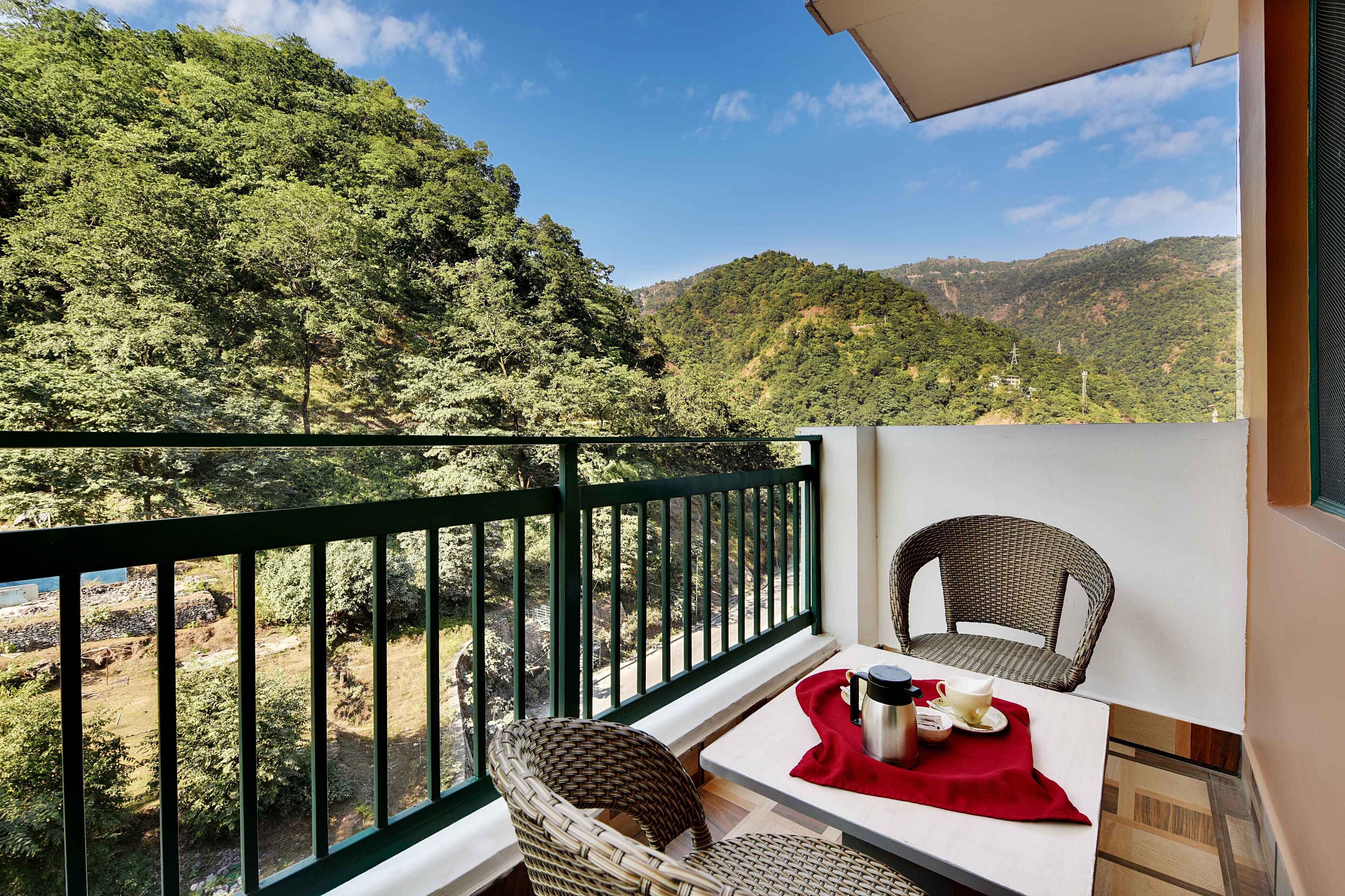 A balcony with wicker chairs and a table, overlooking a lush green hillside.