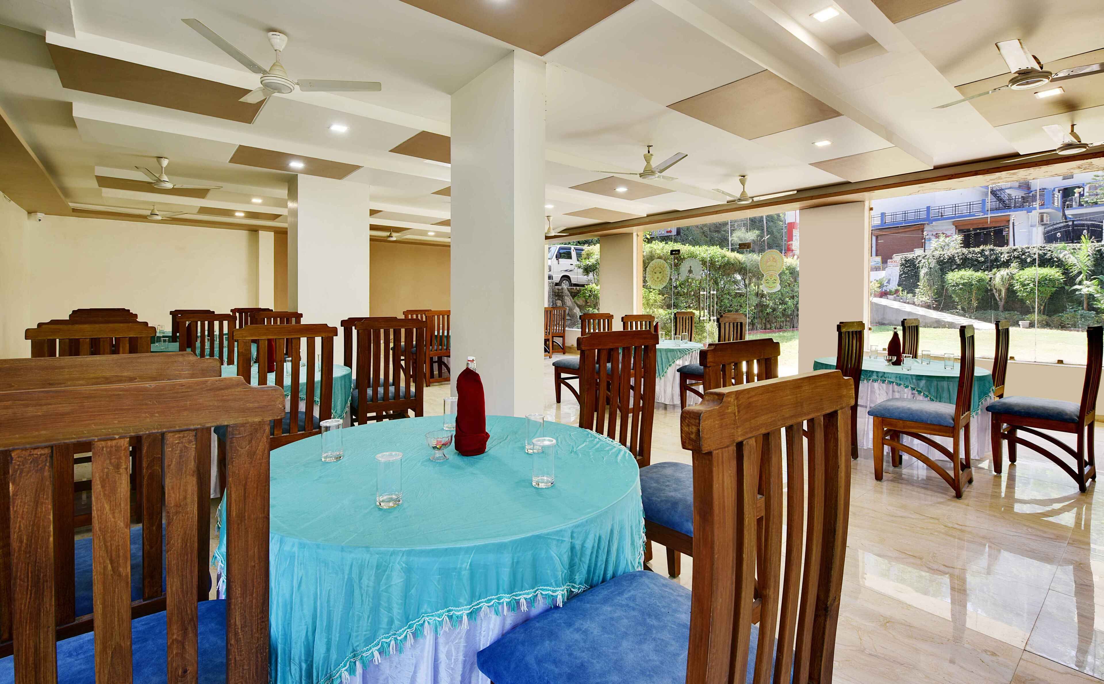 A dining area with round tables covered in blue tablecloths, wooden chairs, and ceiling fans.