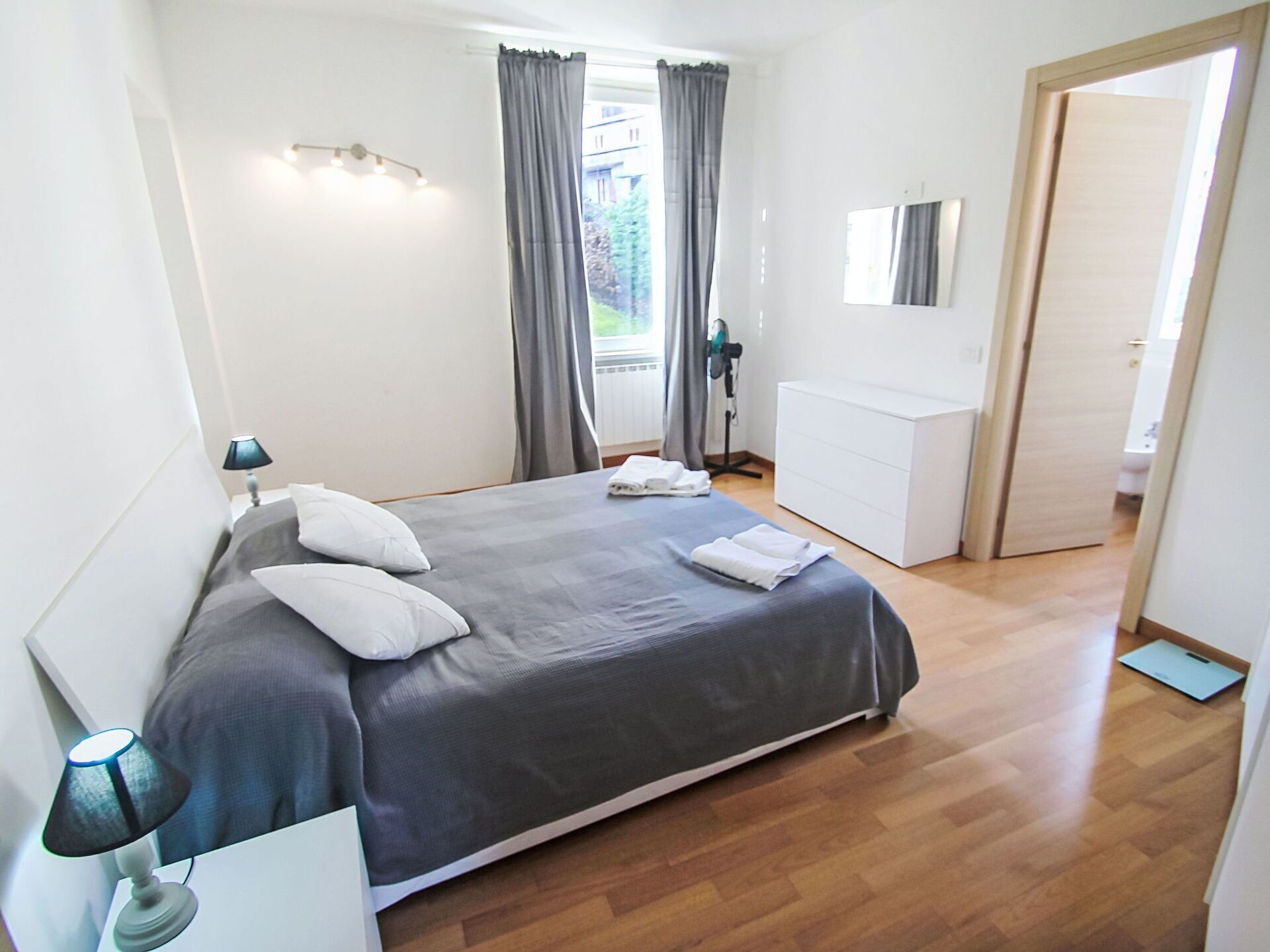Ein modernes Schlafzimmer mit einem großen Bett, einer Nachttischlampe, einem Schminktisch und einem Spiegel an der Wand.