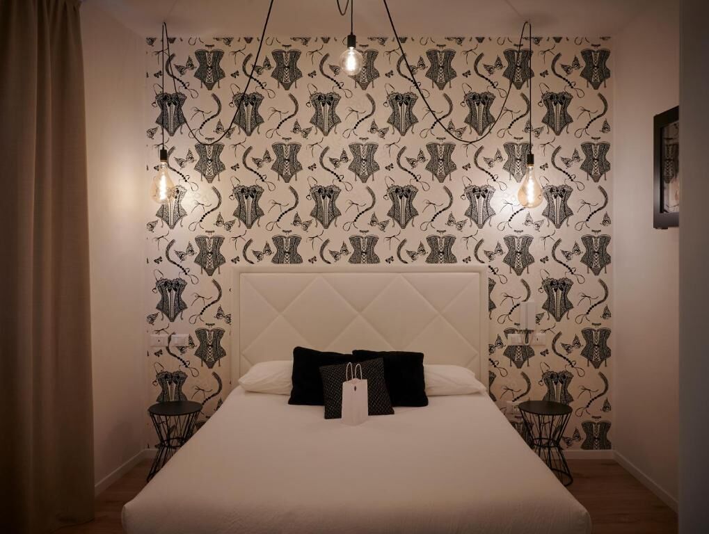 Quarto com papel de parede estampado, cabeceira estofada e mesas de cabeceira com abajures.