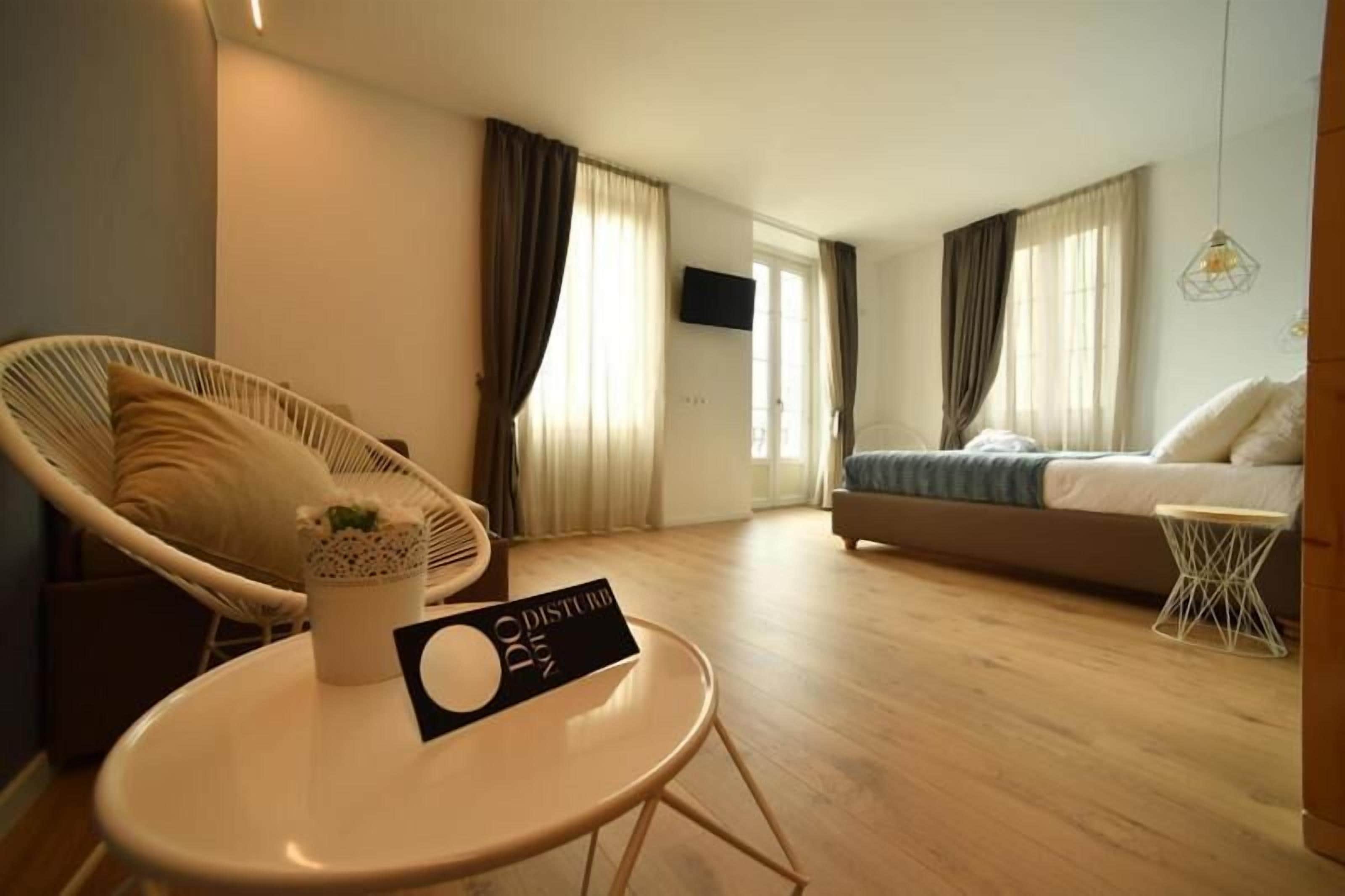 Quarto de hotel moderno com uma cama, uma poltrona, uma mesinha e uma televisão.