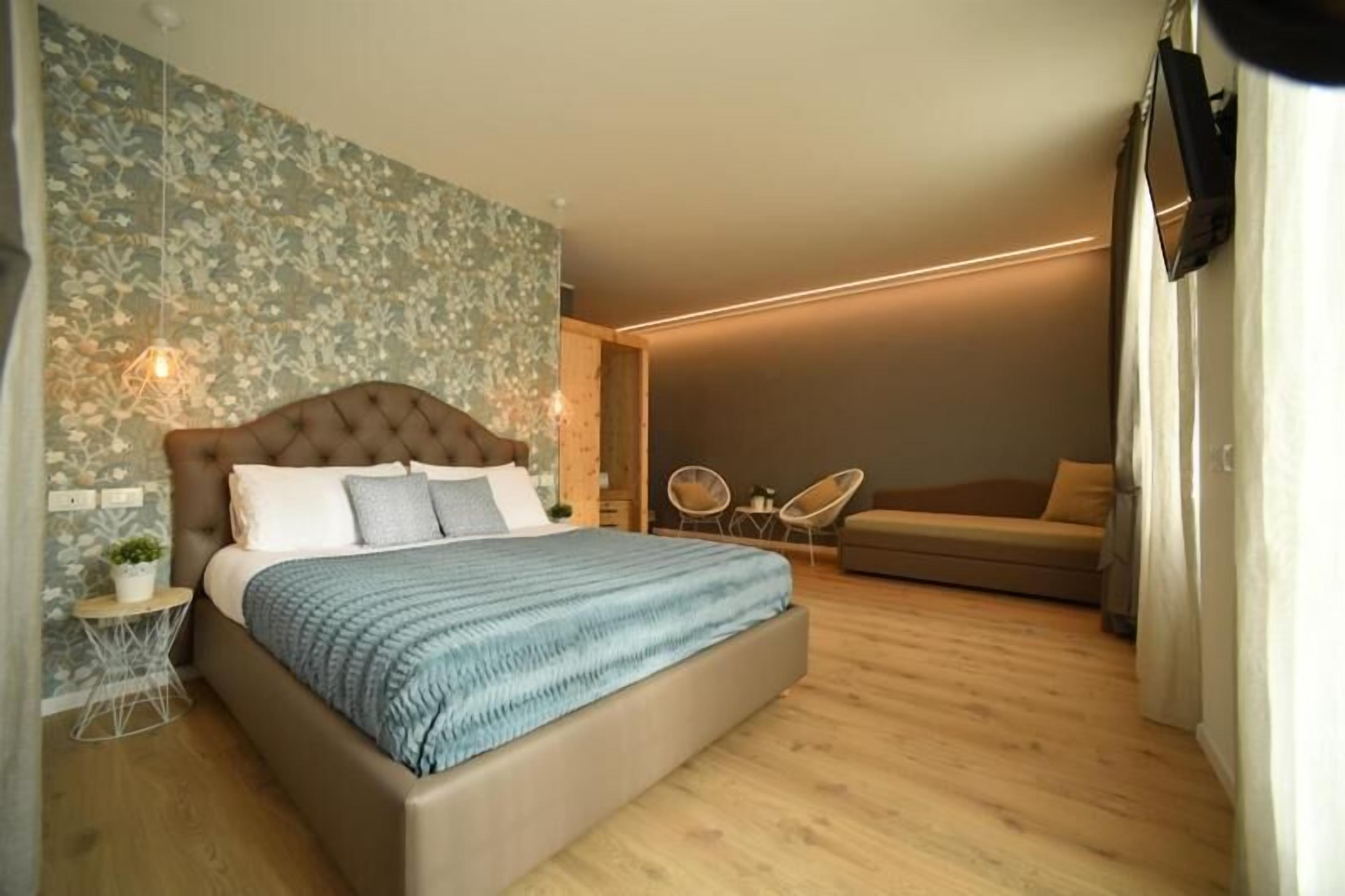 A bedroom with a large bed, a small side table, a wall-mounted TV, and a sofa.