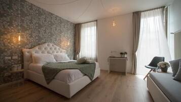 A bedroom with a large bed, a small bedside table, a chair, and a window with curtains.