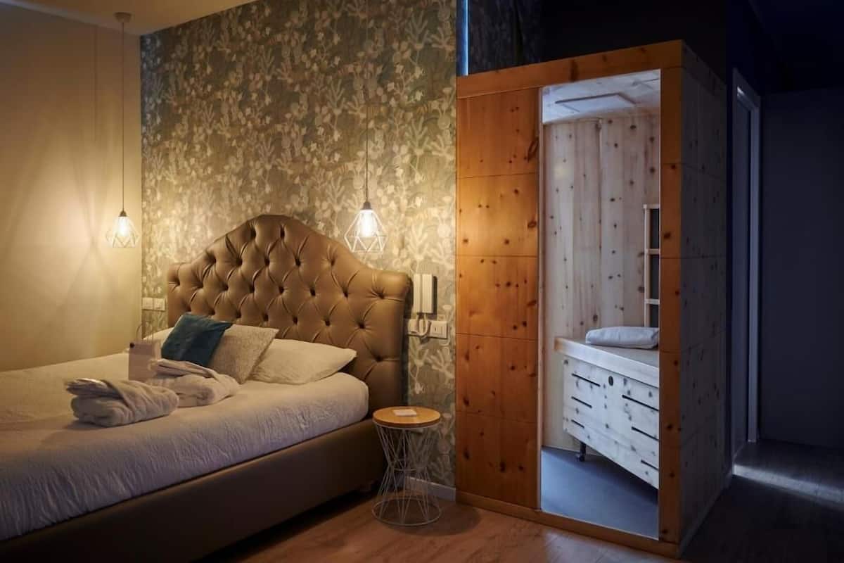 Een slaapkamer met een gestoffeerd hoofdeinde, een nachtkastje en een houten garderobe.