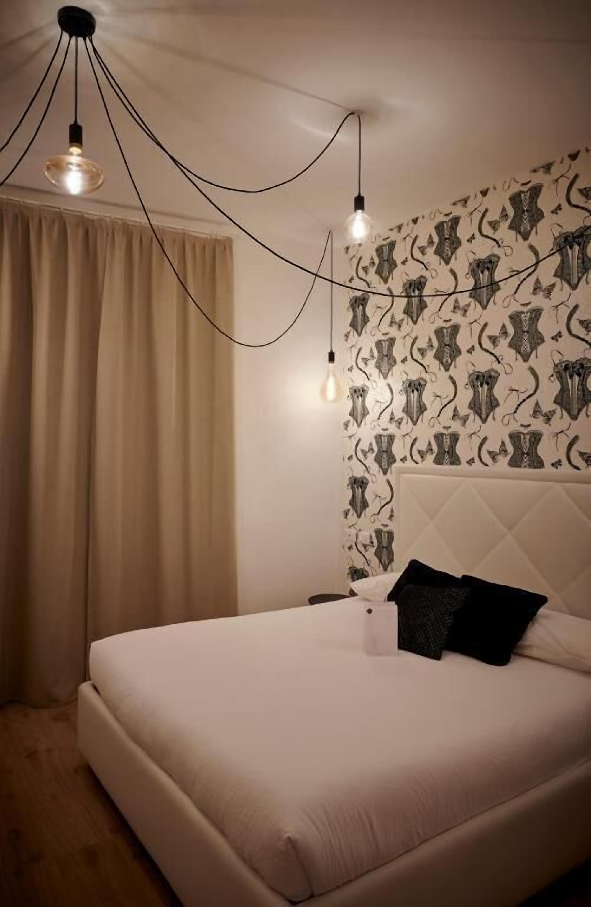 Une chambre à coucher avec un lit, des rideaux, un mur à motifs et des luminaires suspendus.