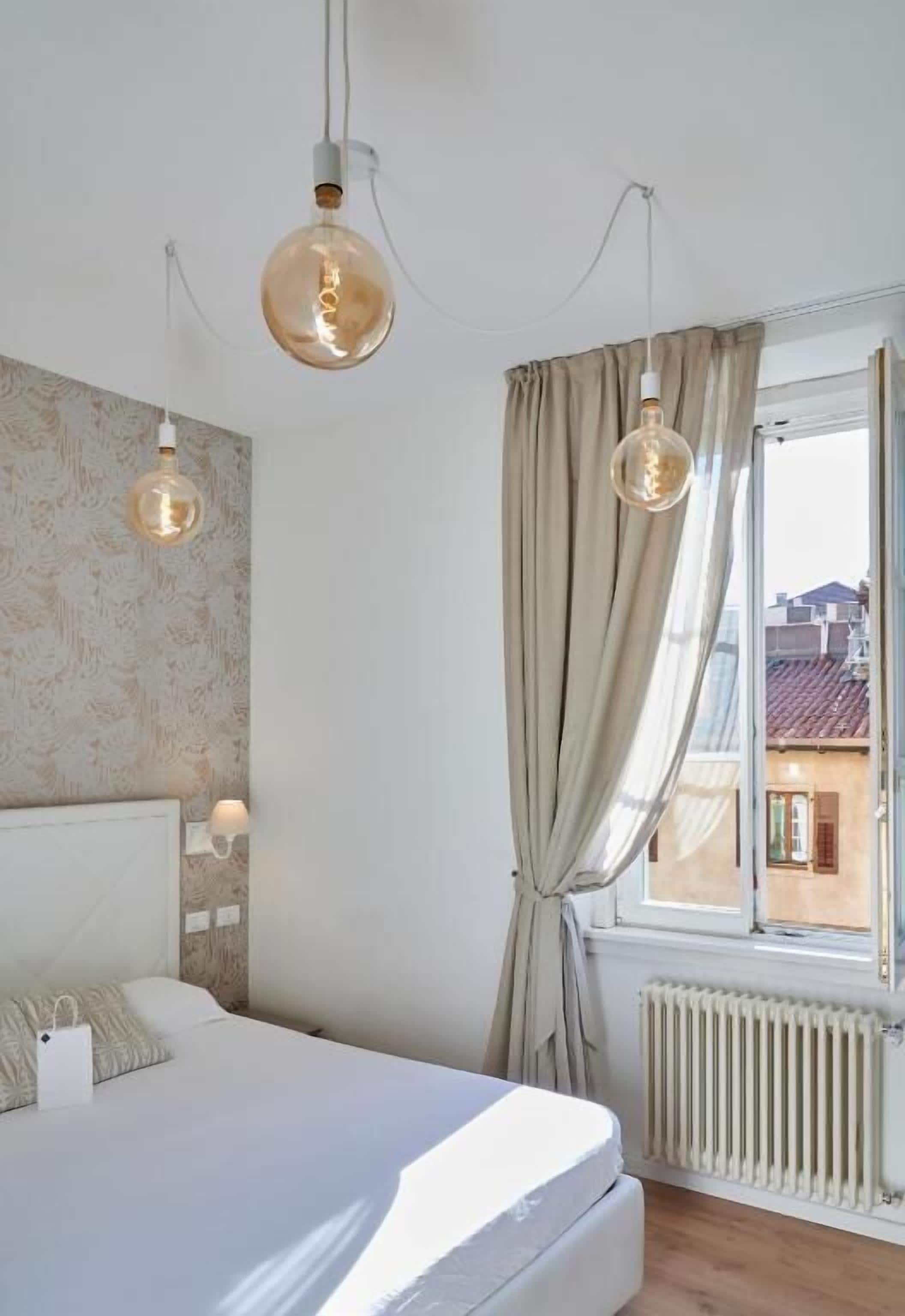 Et soveværelse med en seng, to hængende lamper, et vindue med gardiner og en radiator.
