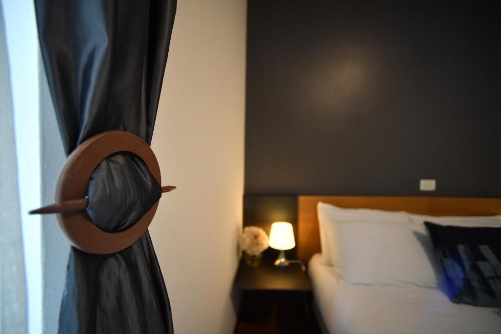 Una habitación de hotel con una cama, una mesita de noche con una lámpara y una cortina con un objeto circular.