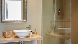 Ein Badezimmer mit einer gläsernen Duschkabine, einem großen Spiegel und einem Waschbecken mit weißer Schüssel.