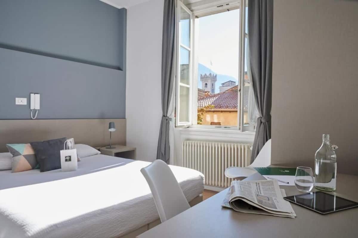 Hotelkamer met een bed, een tafel met een krant, een glas water en een fles.