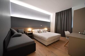 Ein modernes Hotelzimmer mit Bett, Sofa, Schreibtisch und einem großen Fenster mit Vorhängen.