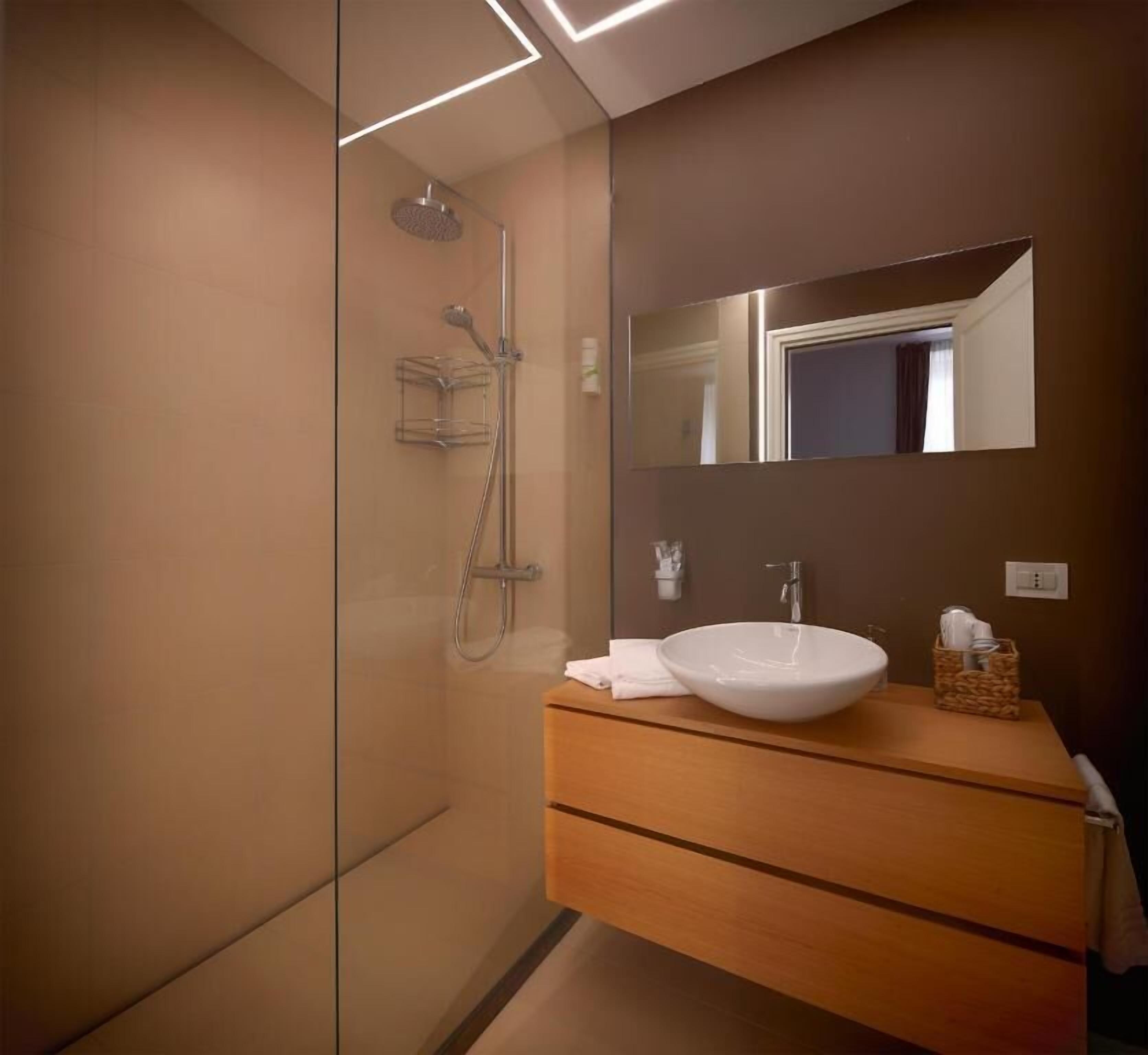 Un bagno moderno con box doccia in vetro, mobile bagno in legno con lavabo bianco e uno specchio grande.