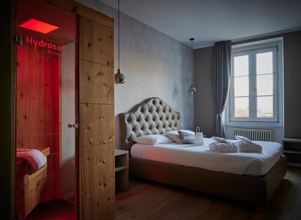 Una camera da letto con una testiera trapuntata, un letto con lenzuola bianche, un comodino, una lampada a sospensione e una finestra con tende.