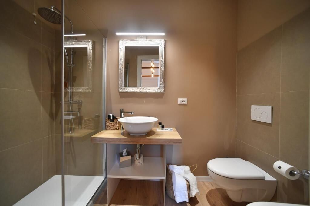 A bathroom with a glass-enclosed shower, a white sink with a mirror above it, and a toilet.