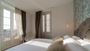 Ein Schlafzimmer mit Bett, Vorhängen, einem Sessel, einem Fenster und einer Wand mit Muster.
