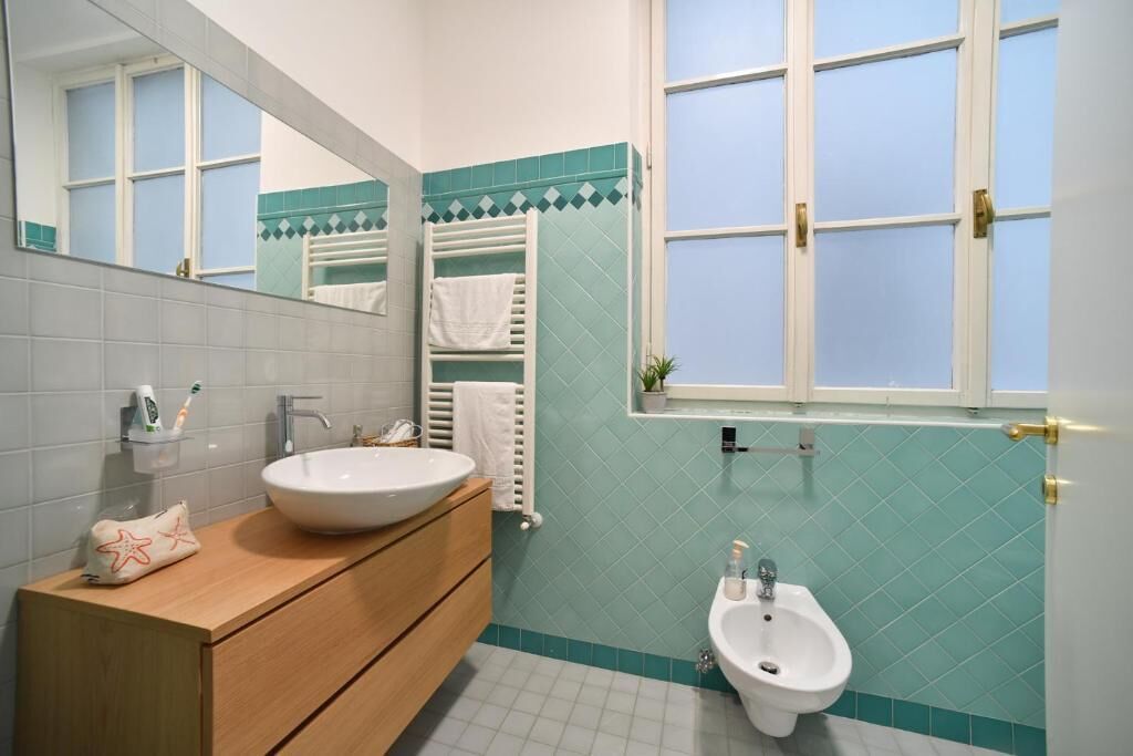 A bathroom with a sink, vanity, bidet, and a window.