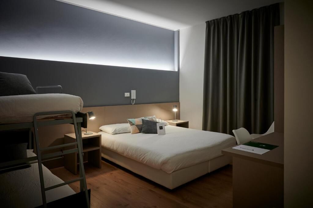 Un dormitorio con una cama litera, un escritorio, una mesita de noche y una lámpara de noche.