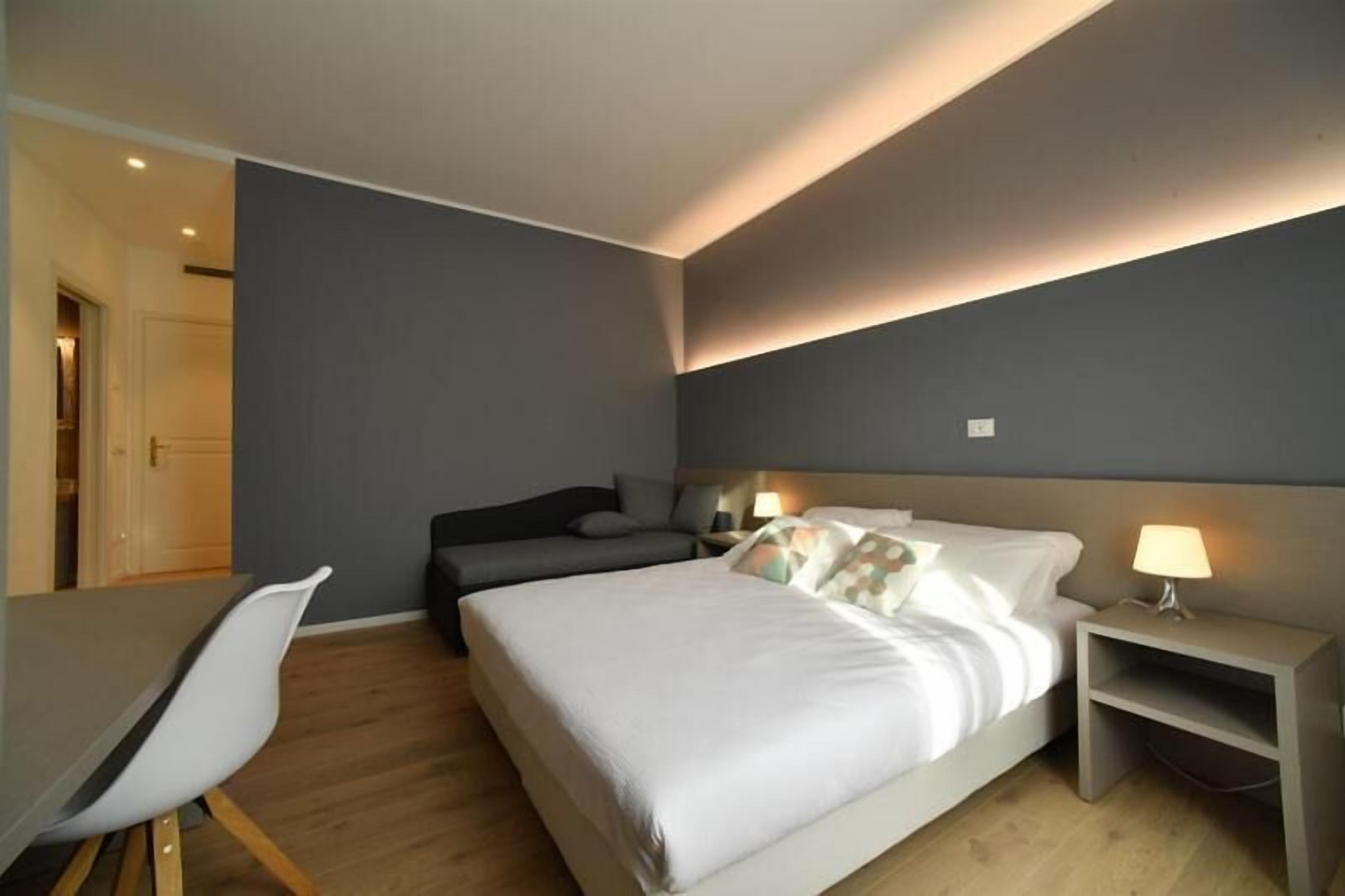 Ein modernes Hotelzimmer mit Bett, Nachttisch, Stuhl und Schreibtisch.