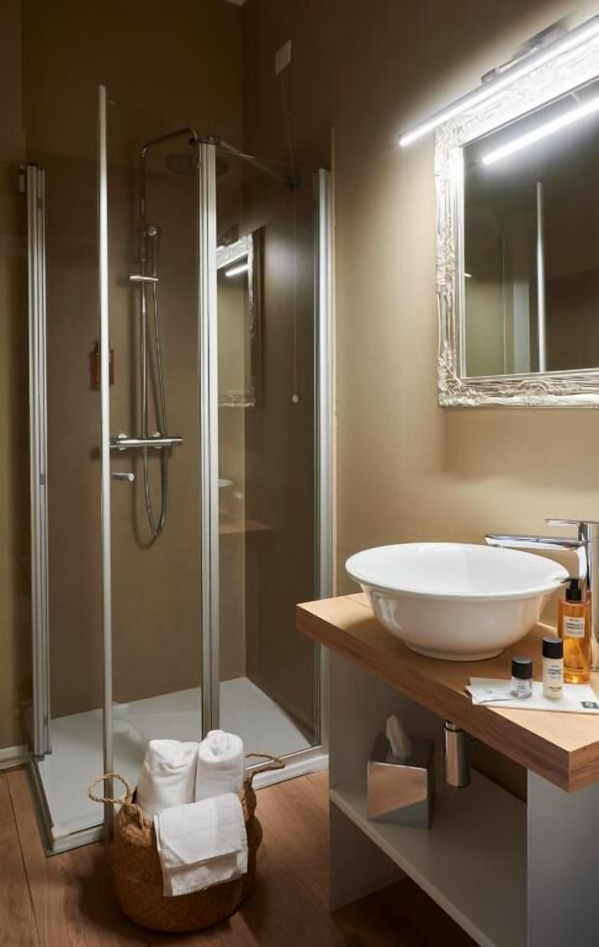 Un baño moderno con ducha envuelta en vidrio, un espejo grande y un tocador de madera con lavamanos blanco.