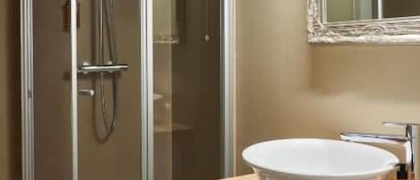 Un baño moderno con ducha envuelta en vidrio, un espejo grande y un tocador de madera con lavamanos blanco.