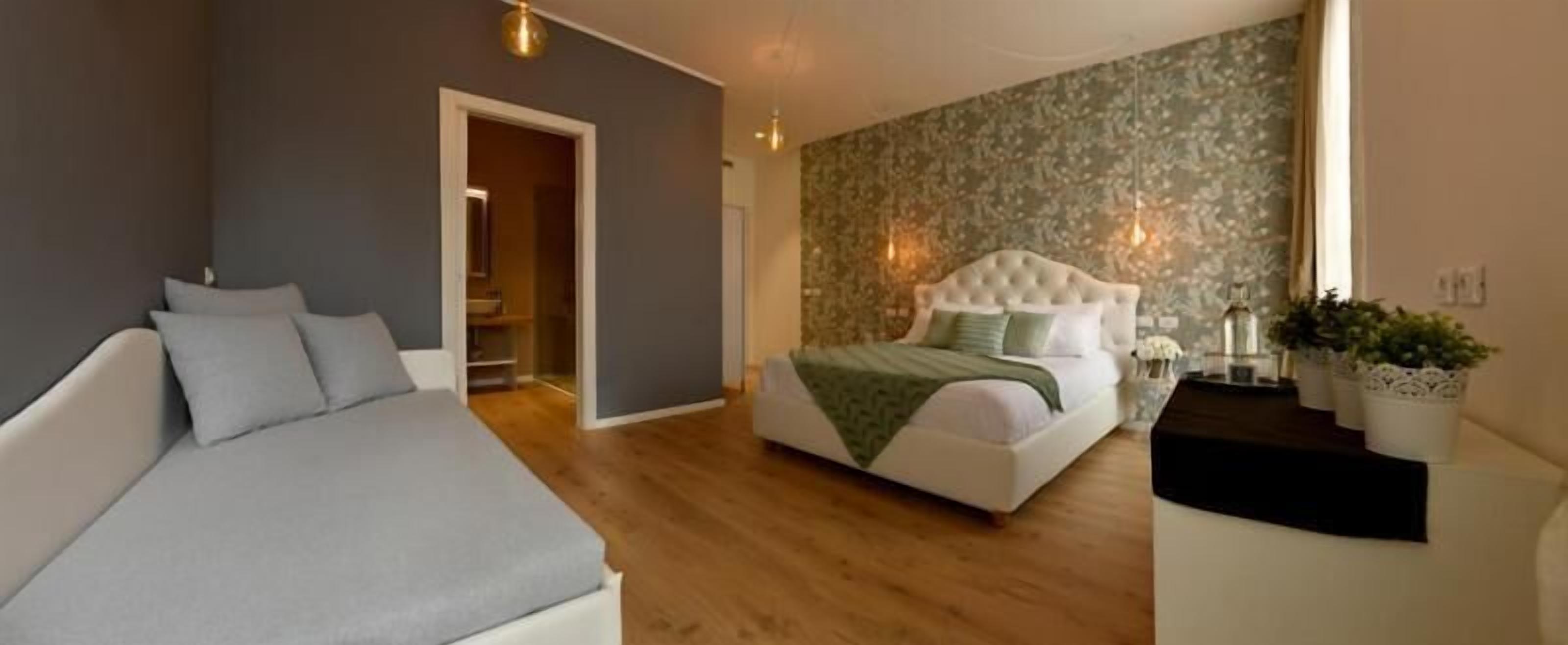 Ein Schlafzimmer mit einem Bett, einer Couch, einem Holzboden, einer Tür und einer Wand mit einem Blumenmuster.