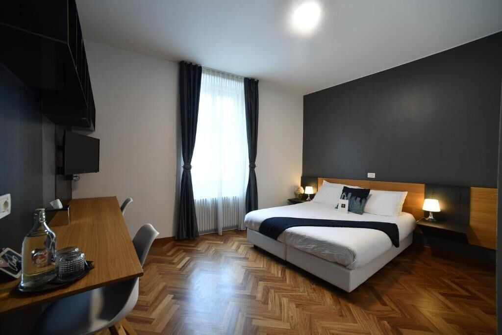 A hotel room with a bed, a desk with a chair, a television, and a window with curtains.