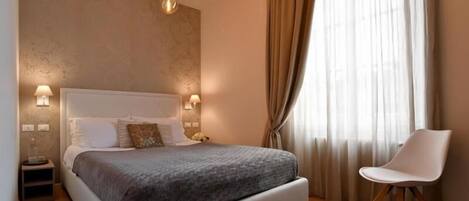 A bedroom with a bed, bedside lamps, a chair, and a window with curtains.