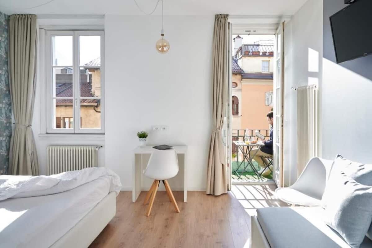 Een slaapkamer met een bed, bureau, stoel en balkon.