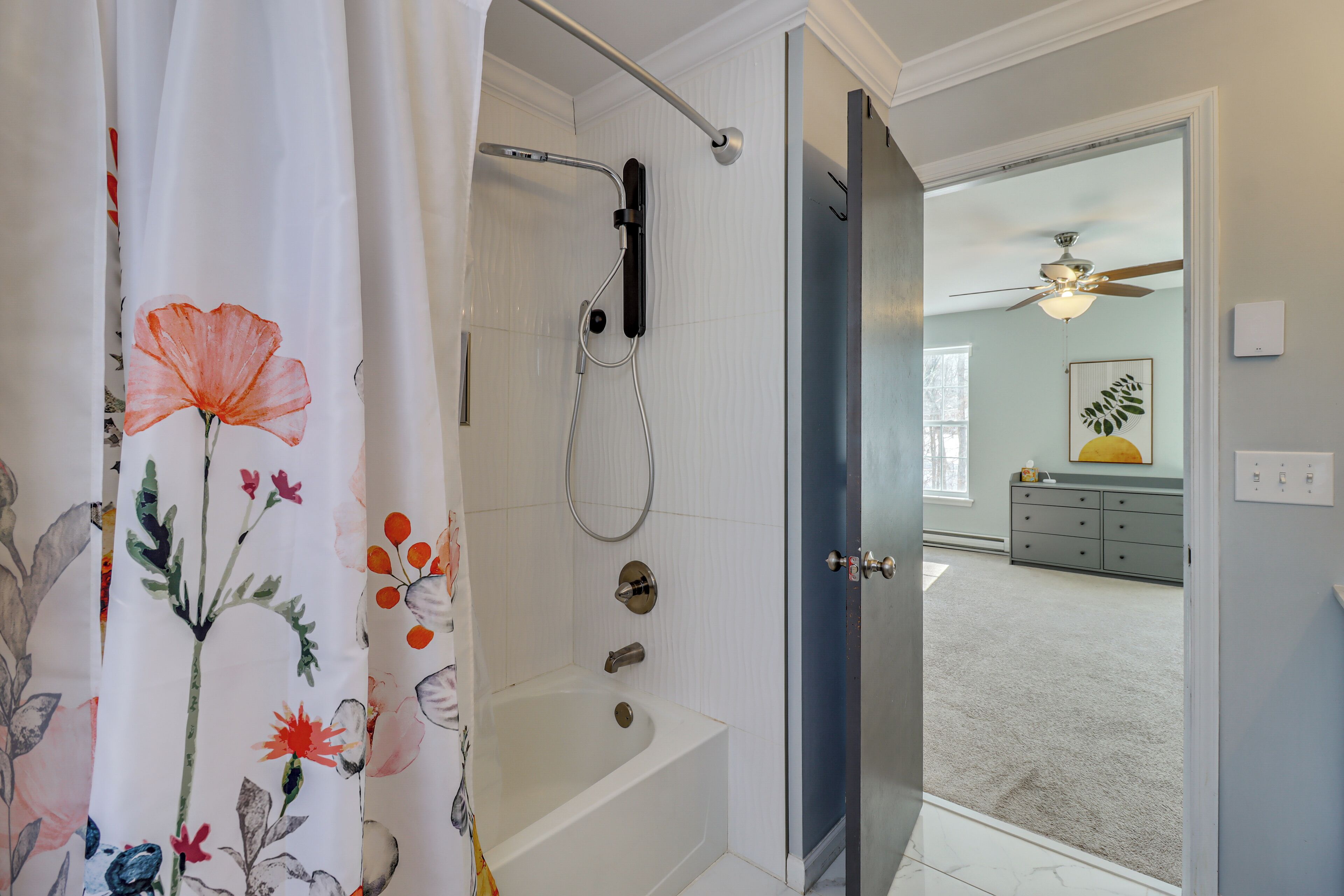 Une salle de bain avec une douche, une baignoire et des toilettes. Une porte donne sur une chambre à coucher qui contient un lit et une commode.