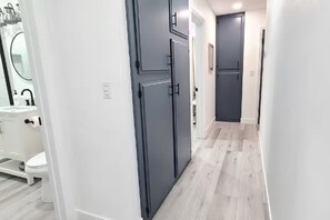 Passadís amb parets blanques i portes grises que condueix a un bany amb un rentapeus i un vàter blancs.