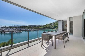 Ein Balkon mit Blick auf einen Yachthafen und Boote, ein Tisch mit Stühlen und eine Tür zu einem anderen Raum.