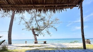 Un pontile di legno con tetto di paglia che si affaccia su una spiaggia con acque cristalline e un albero sullo sfondo.