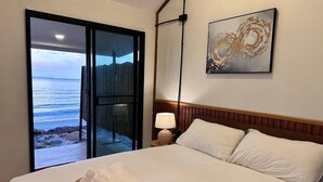 Camera d'albergo con un letto, una lampada da comodino, un'opera d'arte a parete e vista sulla spiaggia attraverso una porta scorrevole.