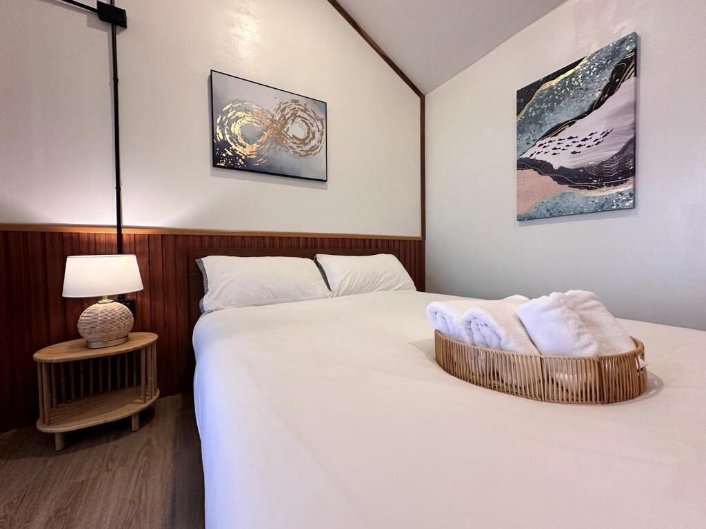 A hotel room with a large bed, a bedside table with a lamp, and two wall-mounted paintings.