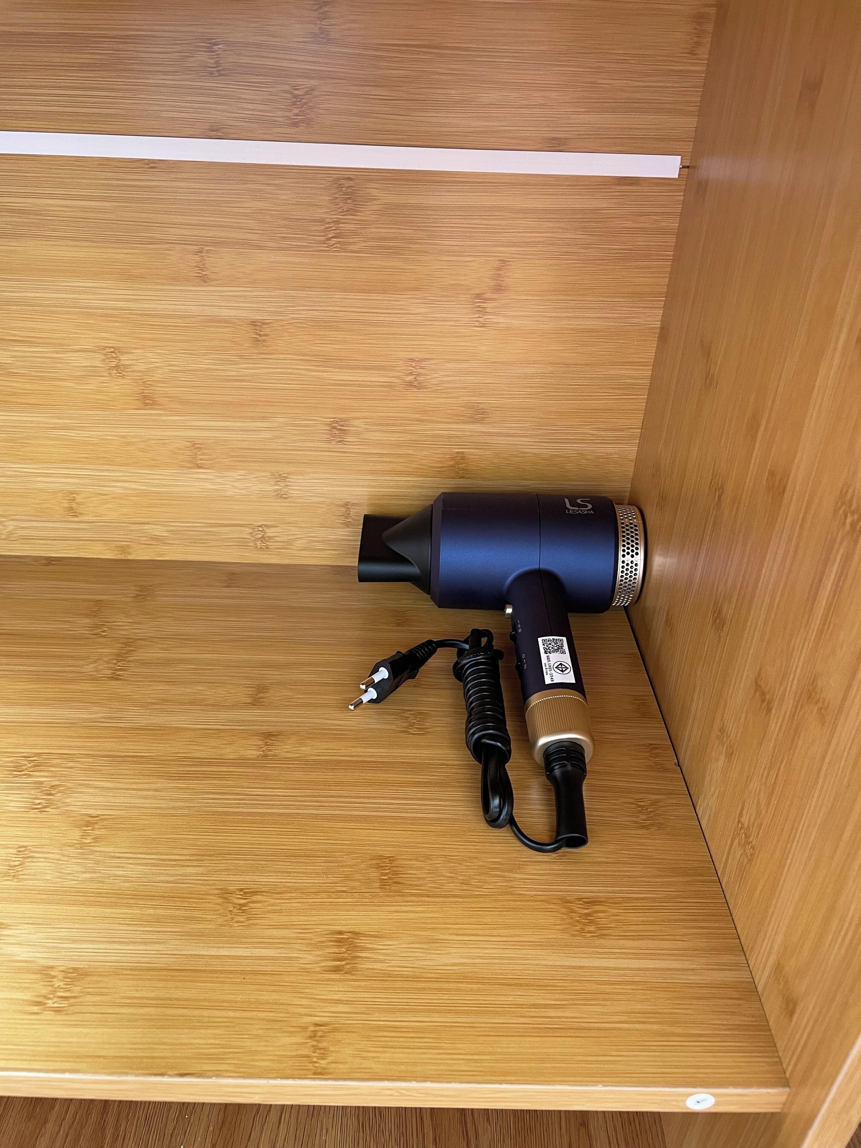 A black hairdryer with a cord and power adapter on a wooden surface.