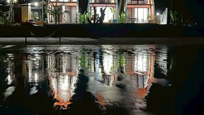 Une rangée de trois structures voûtées, surmontées de toits en bois, bordant un plan d’eau, de nuit.
