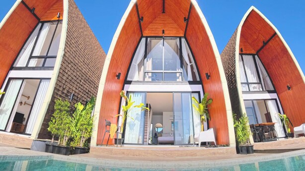 Un edificio moderno con un originale tetto triangolare, ampie finestre e una zona piscina.
