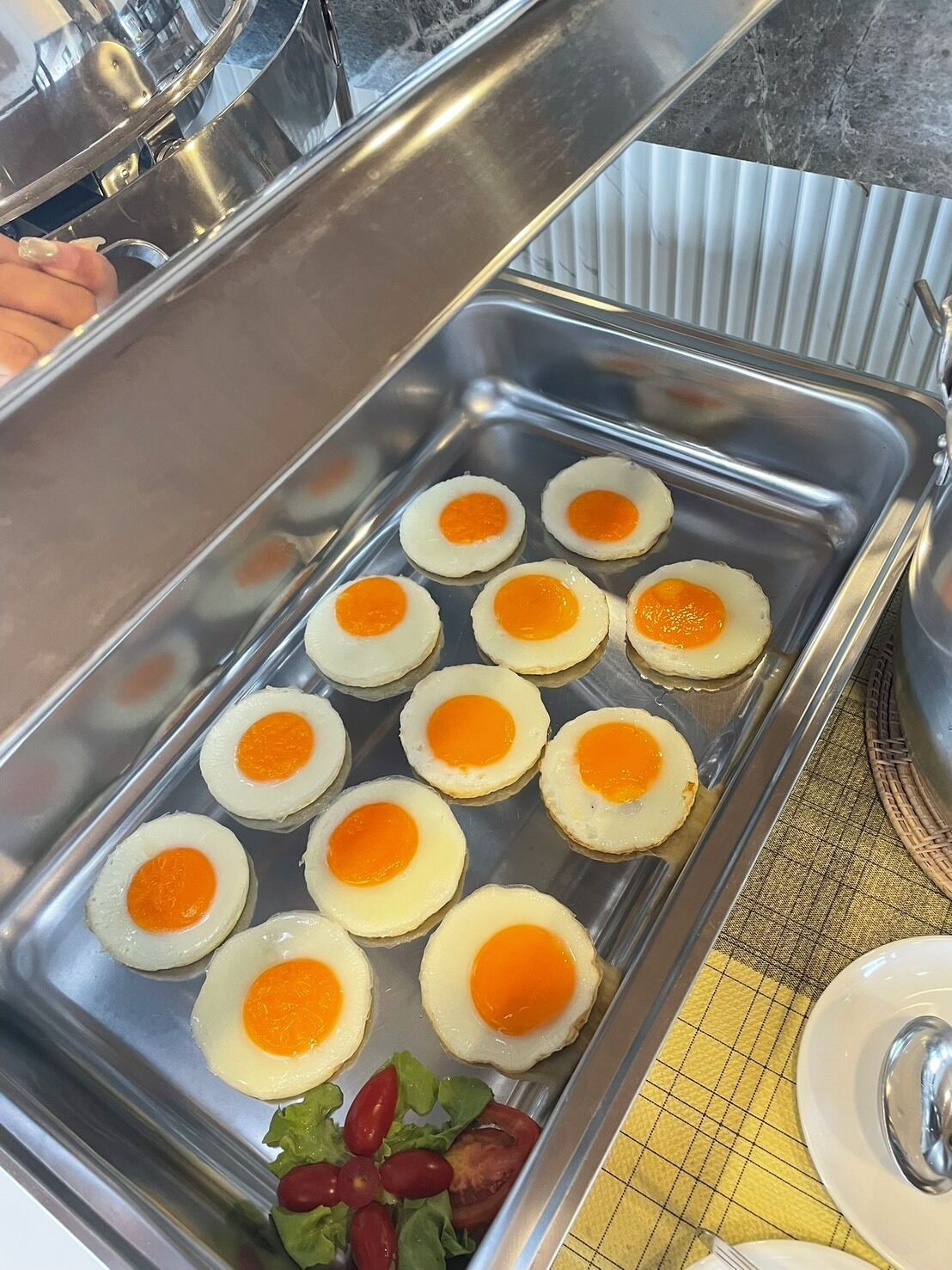 A buffet tray with several sunny-side-up eggs and a small salad of lettuce and tomatoes.
