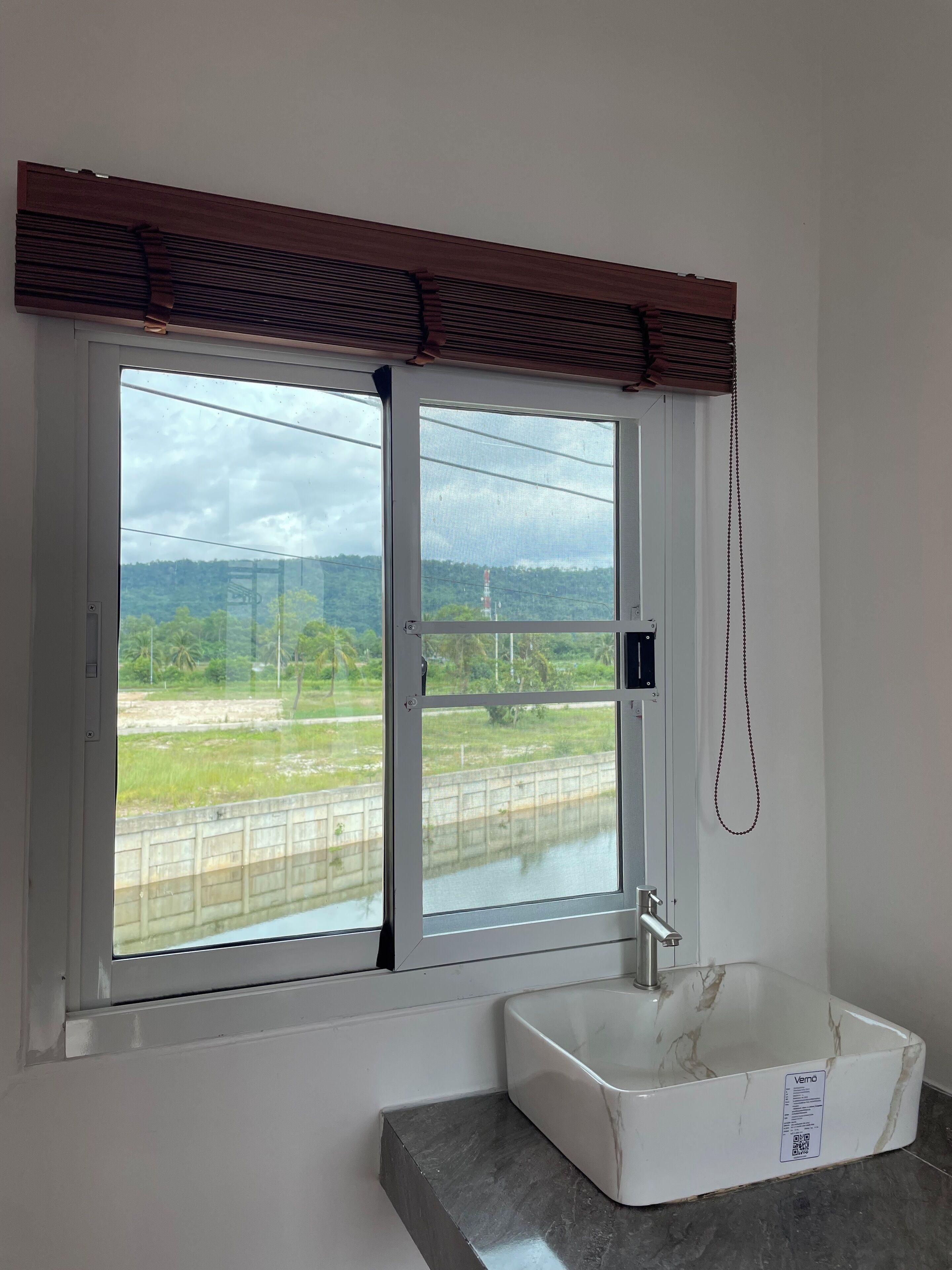 Une salle de bain dotée d’une grande fenêtre, d’un lavabo blanc et offrant une vue sur un paysage verdoyant.