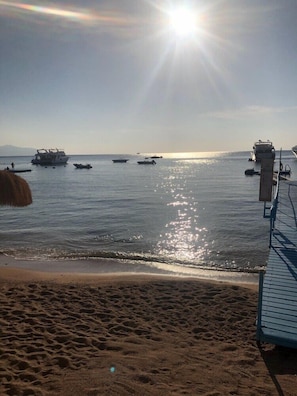 Una playa con barcos en el agua, un muelle y cielo despejado.