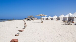 A beach with white tents, a hammock, and a thatched umbrella. - Marsa Shagra Village (Marsa Alam)