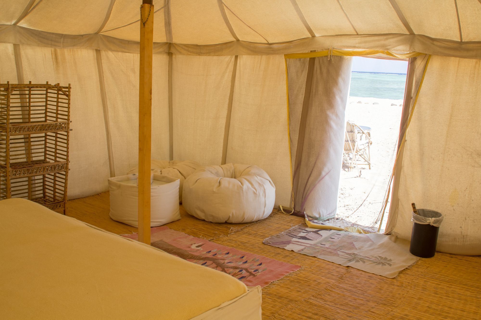 Una habitación con carpa, una cama, un estante de madera, un sillón de peluche blanco y vistas a la playa.