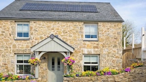 Een stenen huis met een grijze deur, zonnepanelen op het dak en bloembakken rond de ingang.
