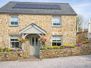 A stone house with a grey door, solar panels on the roof, and flower boxes around the entrance. - The Pump House - UK50648 (Falmouth)