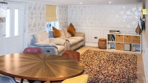 Een gezellige woonkamer met een ronde houten tafel, een bank en een kleurrijk vloerkleed.